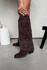 Brown suede pants with rhinestone details worn by a person, standing on a gray floor.