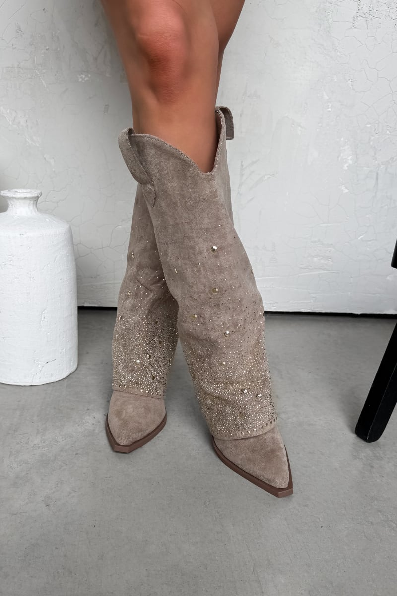 Beige ankle boots with pearl embellishments worn by a person on a light gray floor.