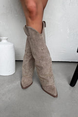 Beige ankle boots with pearl embellishments worn by a person on a light gray floor.