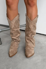 Beige suede Western cowboy boots worn by a person on a light gray floor. ETTA Studded Slouched Cowboy Western Boots - Beige Suede - 5