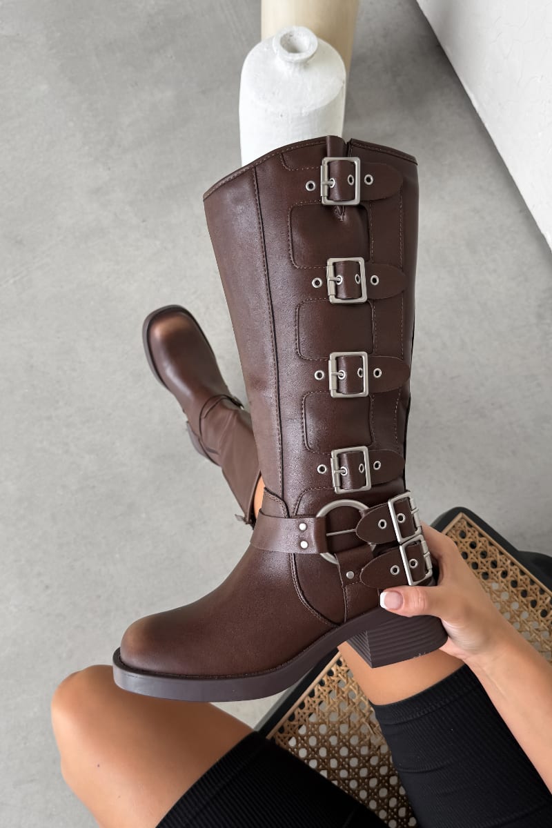 Brown knee-high boots with buckles held by a person on a gray surface