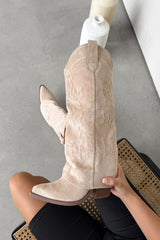 Beige suede cowboy boot held by a hand on a neutral background