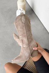 Beige knee-high boot held by a person on a gray surface