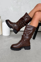 Brown knee-high boots with buckles worn by a person sitting on a chair.