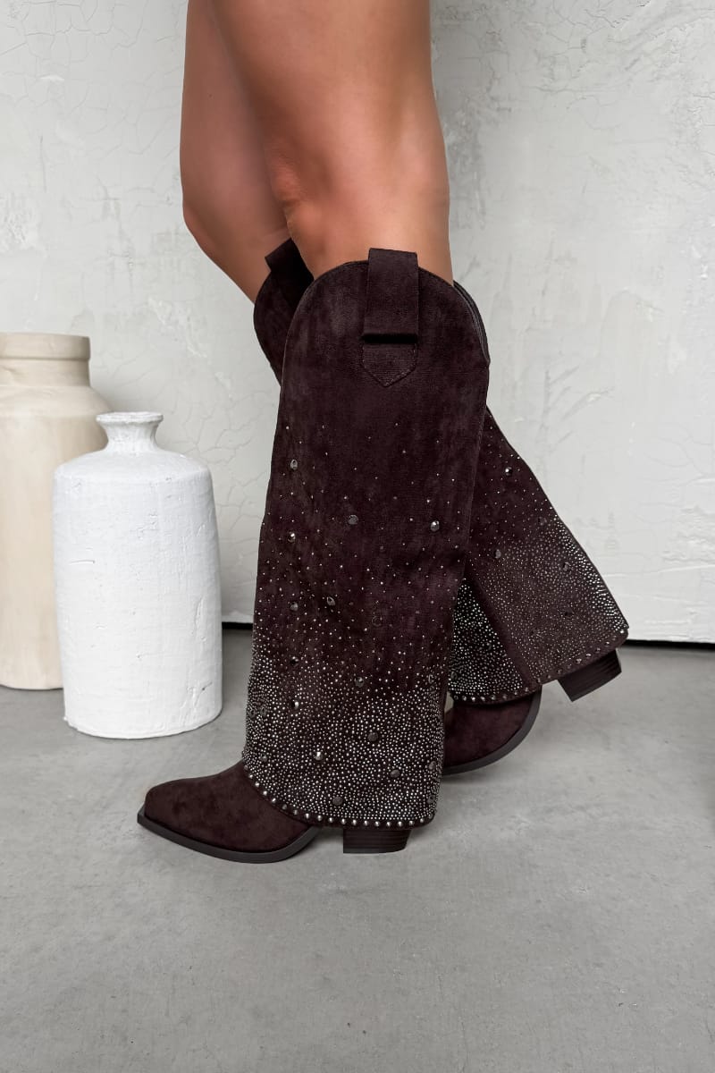 Brown suede boots with rhinestone details worn by a person, against a neutral background.