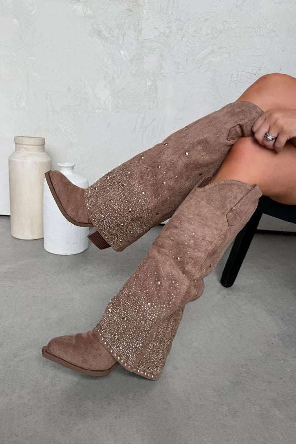 Camel knee-high boots with embellishments worn by a person sitting on a chair.