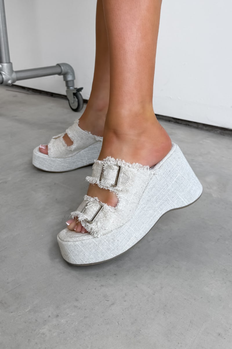 White platform sandals with frayed edges worn by a person on a concrete floor. DEMI Woven Buckle Wedge Sandals - Beige - 2