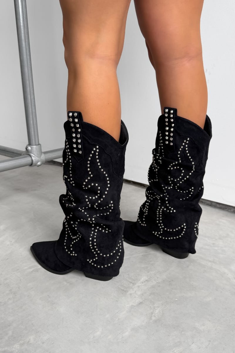 Black western cowboy studded boots worn by a person on a concrete floor. ETTA Studded Slouched Cowboy Western Boots - Black Suede