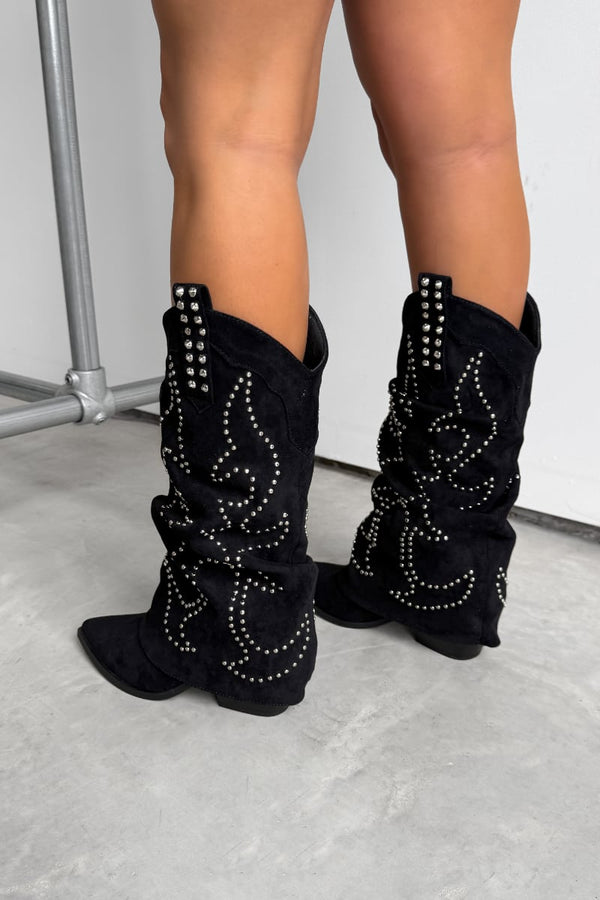 Black western cowboy studded boots worn by a person on a concrete floor. ETTA Studded Slouched Cowboy Western Boots - Black Suede