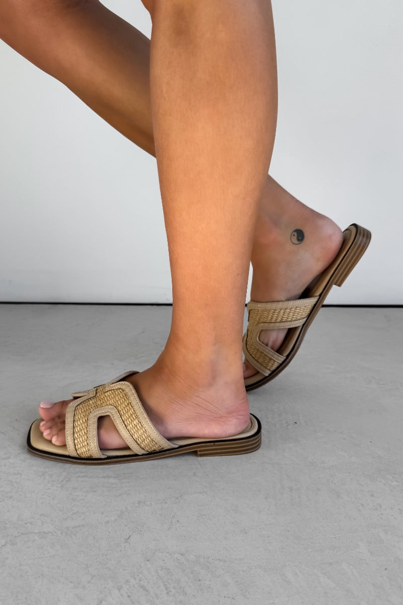 Beige sandals worn on feet against a neutral background