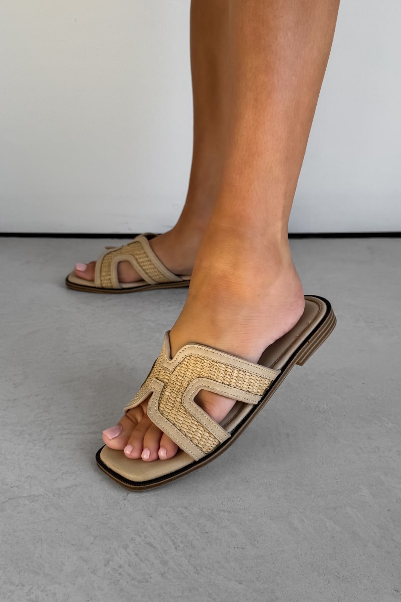 Beige sandals worn on feet against a neutral background