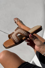 Brown embellished sandal held by a hand against a neutral background