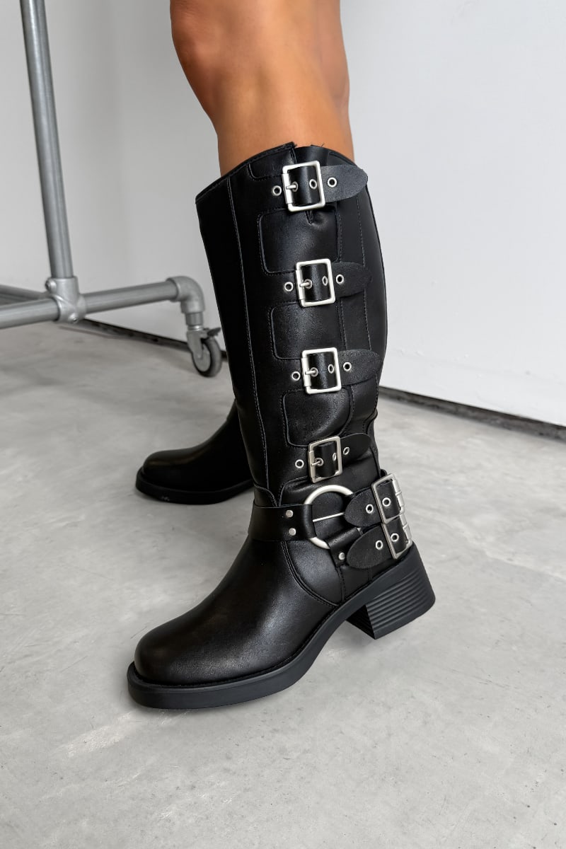 Black knee-high boots with multiple buckles on a light gray floor. GEORGIA Chunky Buckle Biker Boots - Black. - 1