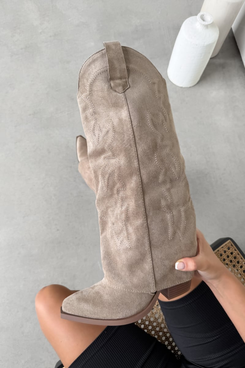 Beige suede knee-high boot held by a person on a gray floor.