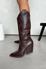 Brown cowboy boots on a light gray floor with a white wall background