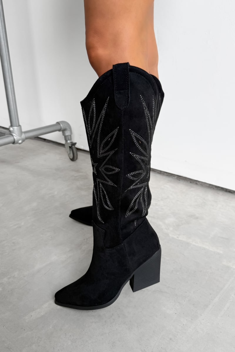 Black knee-high western cowboy boots with a traditional design worn by a person on a light gray floor - 1