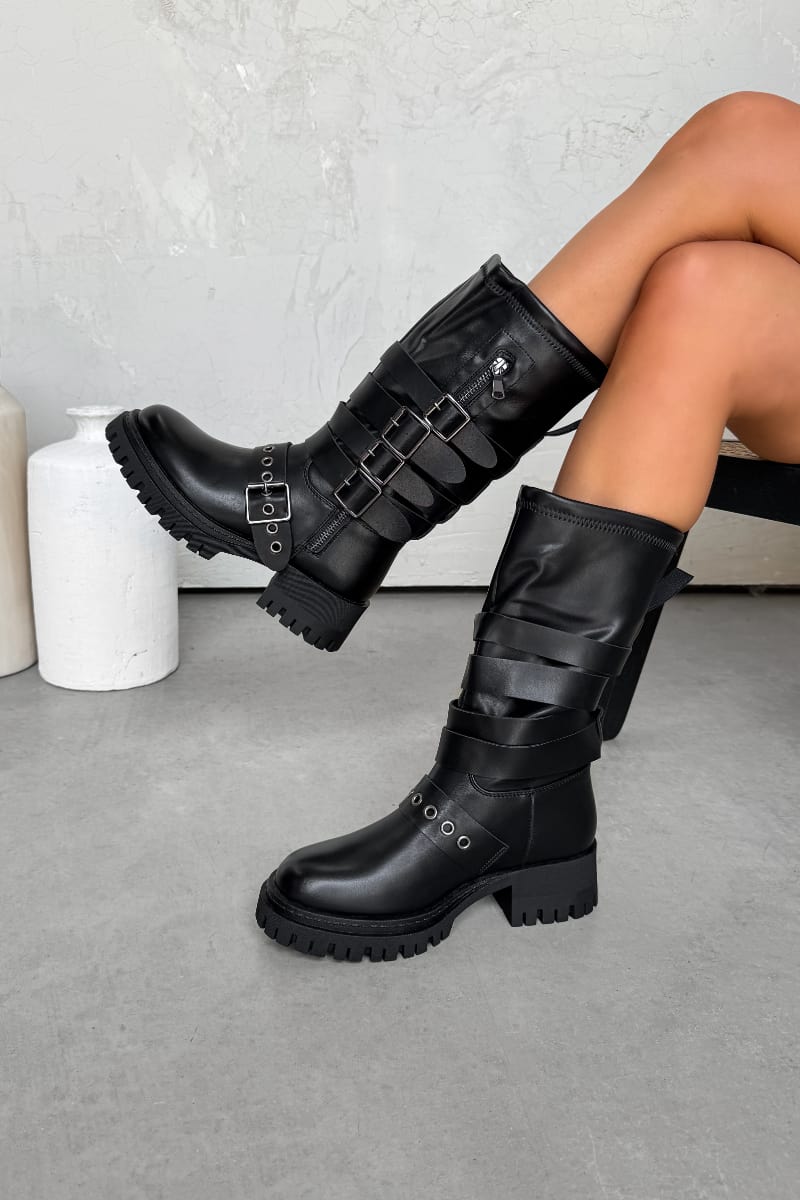 Black knee-high boots with buckles worn by a person on a gray floor.