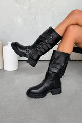 Black knee-high boots with buckles worn by a person on a gray floor.